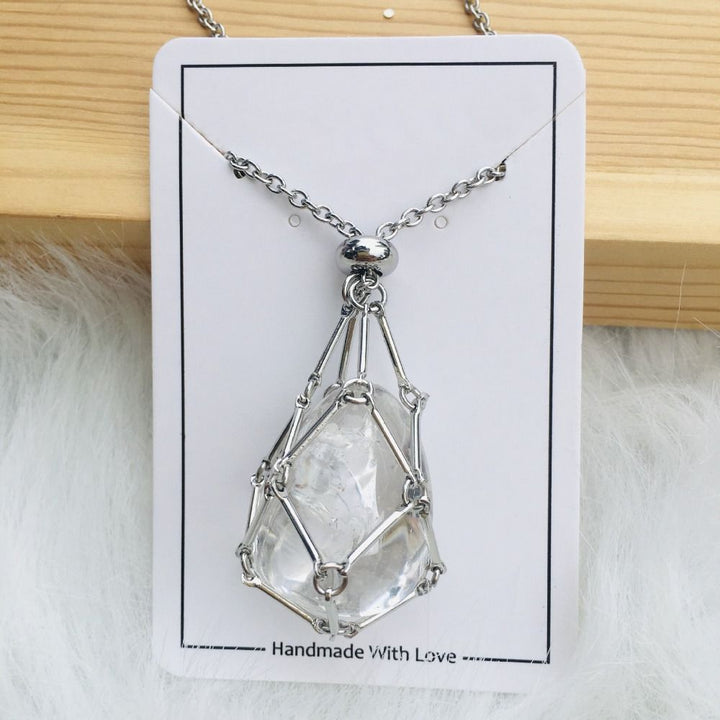 Silver cage necklace with a clear rough-looking quartz stone on a white card with wood and white fur behind. 15