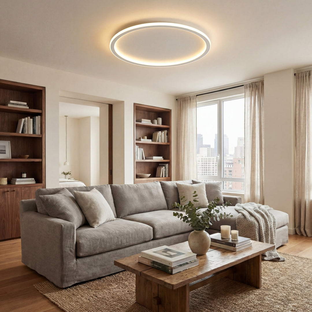 White ring ceiling light in a living room with a gray sectional sofa and wooden bookshelves
