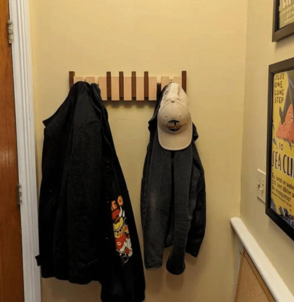 Light wood hook rack mounted in a hallway, holding two dark jackets and a beige baseball cap. 6