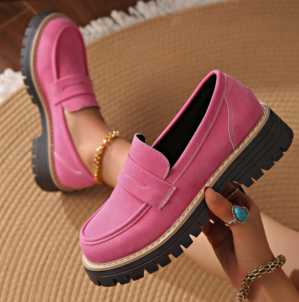 Hot pink loafer held in a hand with a turquoise ring, with another loafer worn on a foot.