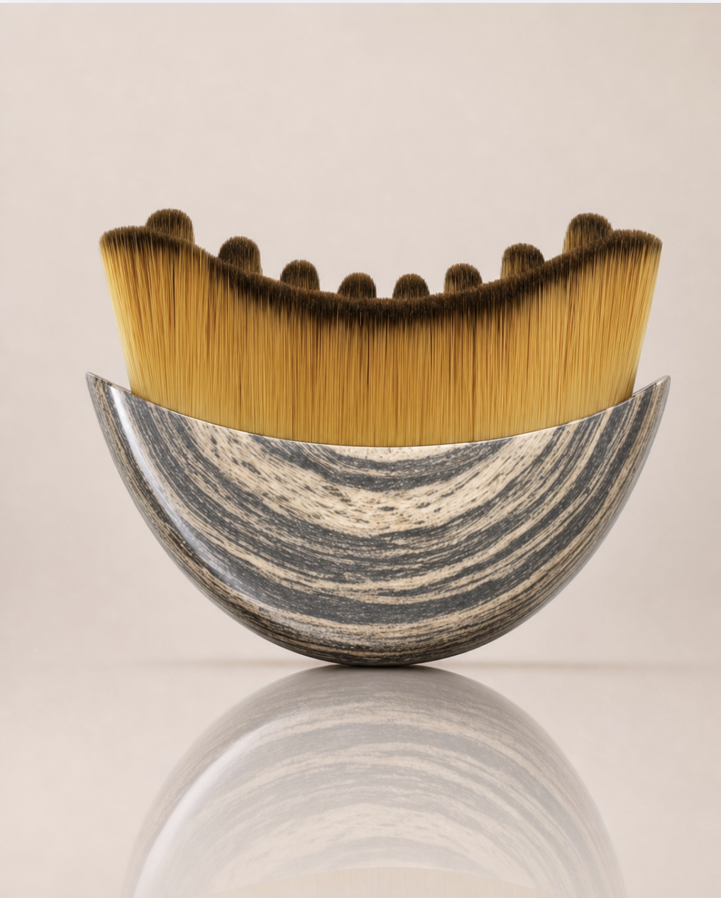 Curved facial massage brush with golden soft bristles and a scalloped top edge, set in a glossy gray and cream marbled handle.