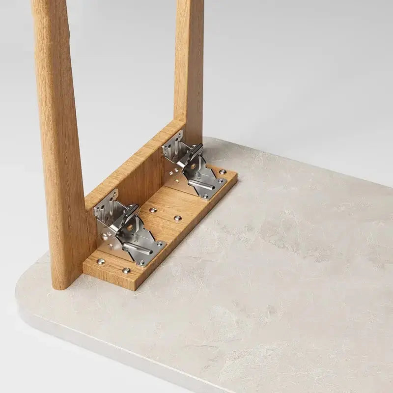 Underside of a table showing two brackets mounted on a wooden cleat, with a leg standing open against a stone-look tabletop. 2