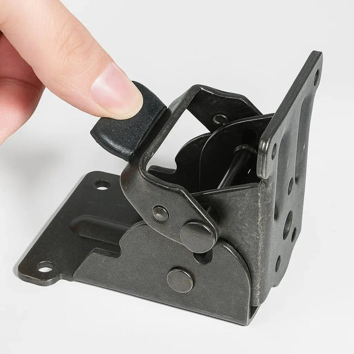 Fingertip pressing the black release tab of a dark gunmetal bracket, which is held at a right angle against a white surface. 9