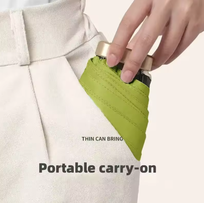 A hand sliding a folded green umbrella with a gold cap into the pocket of cream trousers.