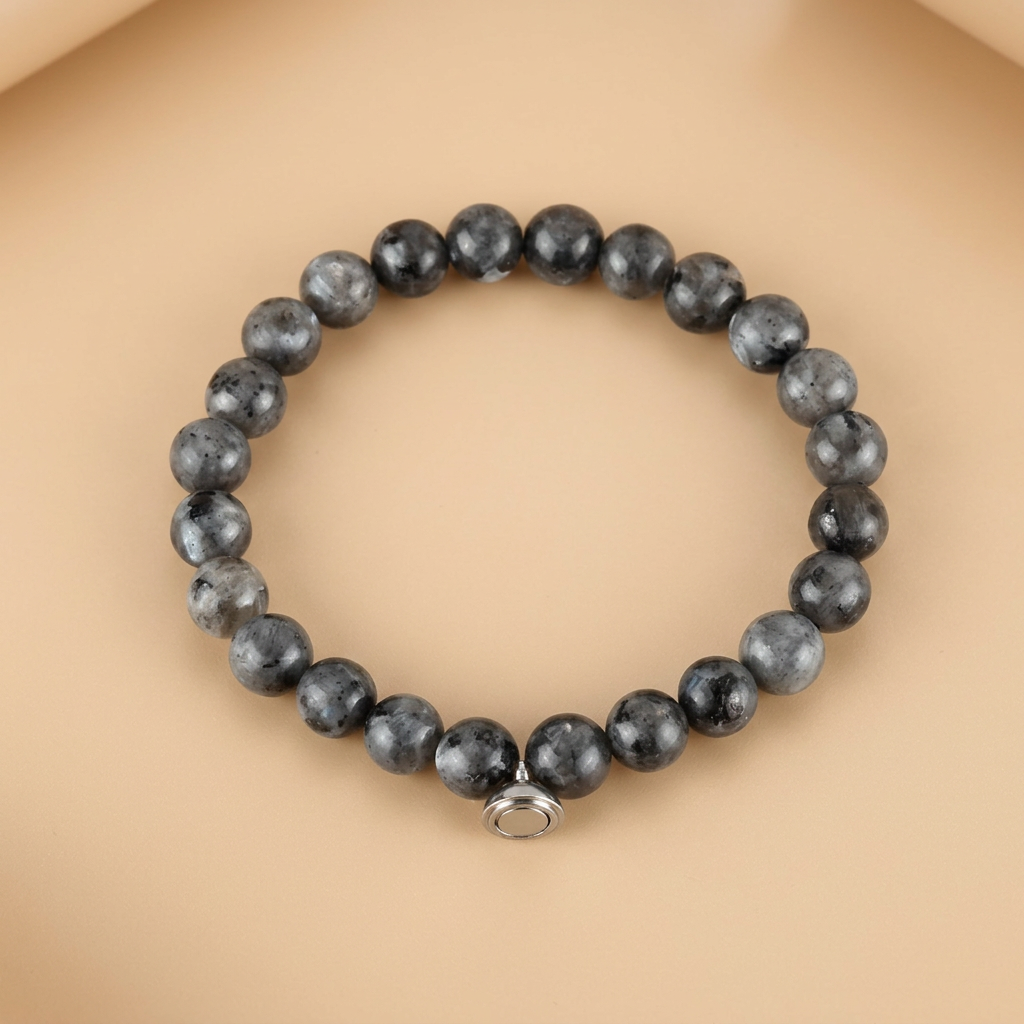 Gray speckled stone bead bracelet with a small round silver magnetic charm, displayed flat on a peach backdrop 4