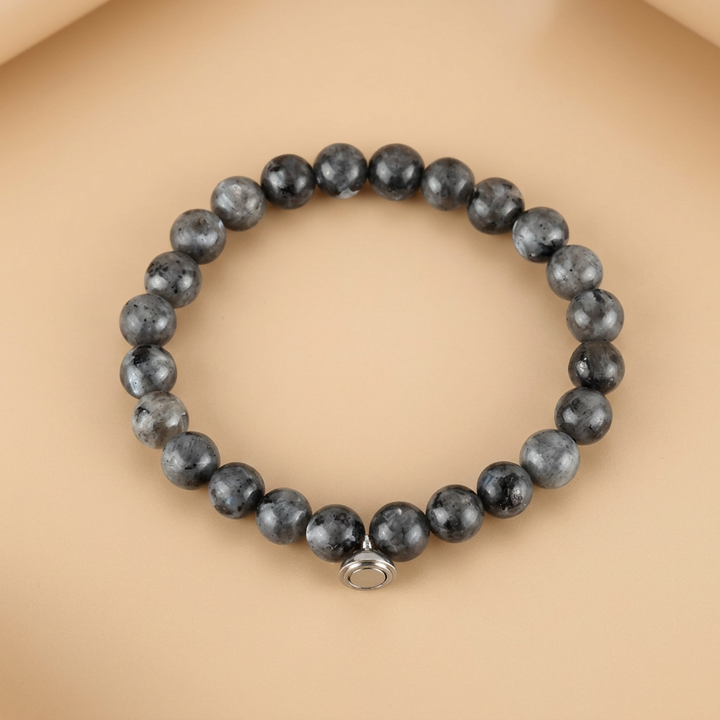 Gray speckled stone bead bracelet with a small round silver magnetic charm, displayed flat on a peach backdrop 4