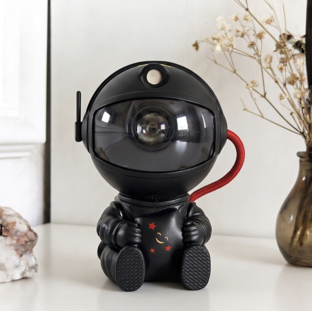 Black astronaut projector with a red braided cord, holding a star with a smiling face, front view.