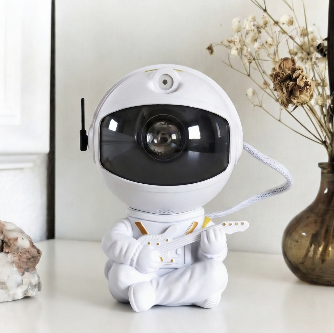 White astronaut projector sitting cross-legged and playing a small guitar, with gold accents and a white cord, front view.