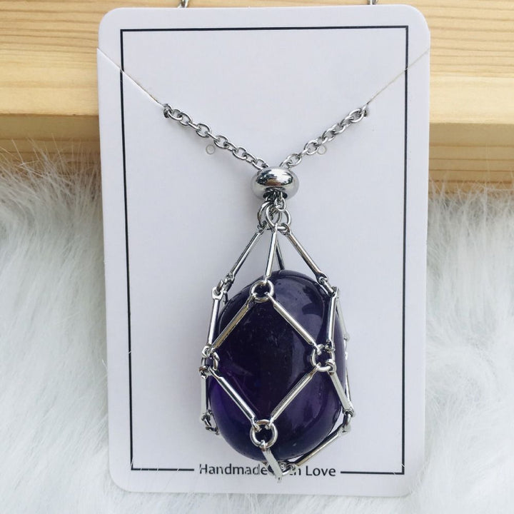 Silver cage necklace with an oval dark purple amethyst stone on a white card against wood and white fur. 17