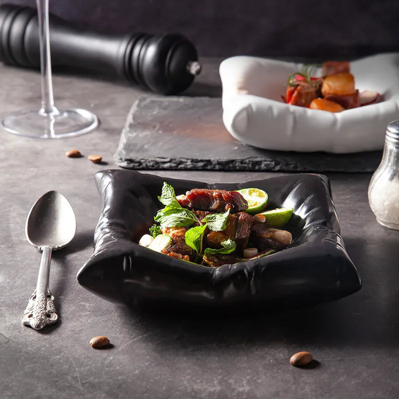 Black cloud-shaped porcelain bowl on a dark table, filled with meat, lime and mint leaves.