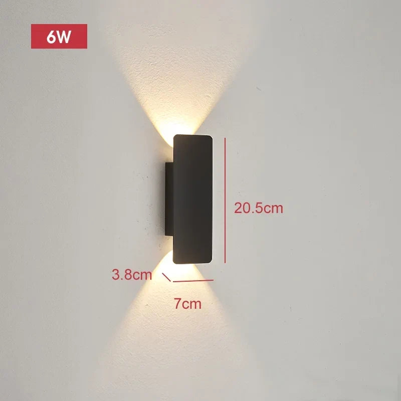 Compact black wall light on a pale wall casting warm light up and down, with dimension lines marking its size.