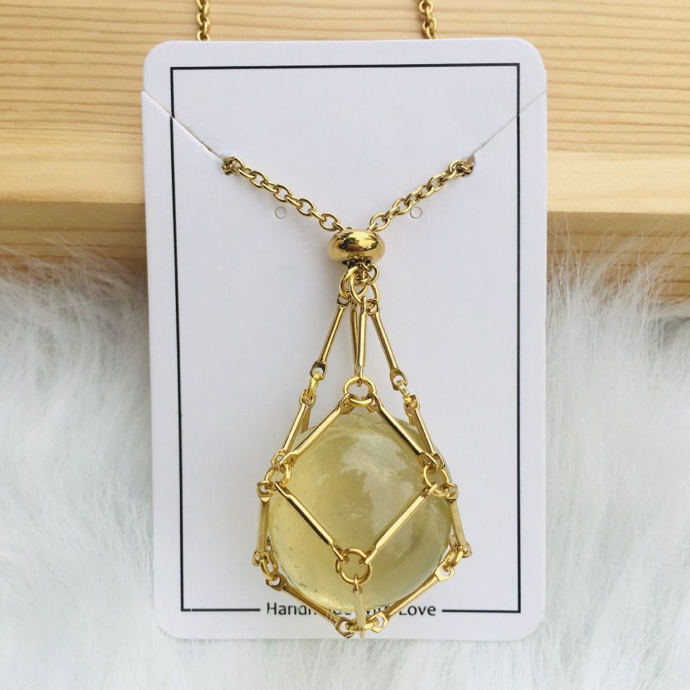 Gold-tone cage necklace with a round pale yellow stone on a white card against wood and white fur. 1