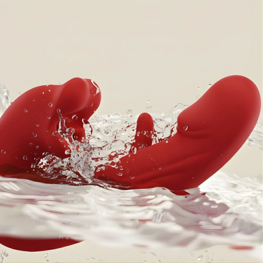 Red silicone massager with curved arms splashing into clear water against a beige background, highlighting its water-resistant design. 1