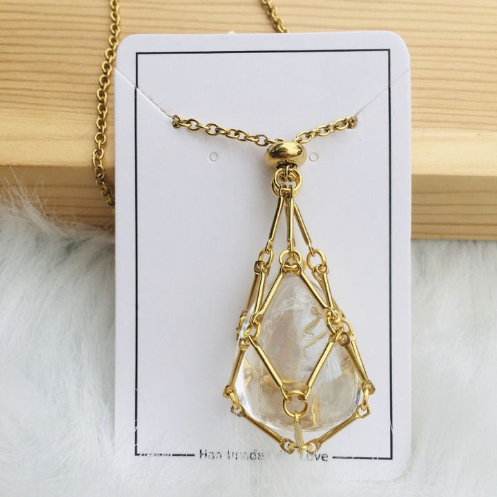 Gold cage necklace with a clear teardrop-shaped quartz stone on a white card against a wood plank. 14