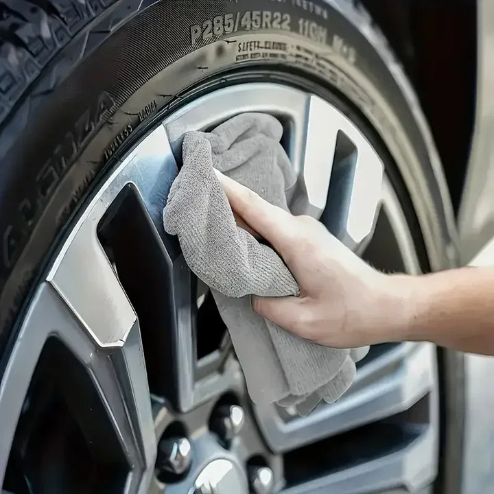 Grey microfiber cleaning cloth wiping a car wheel rim, another view.