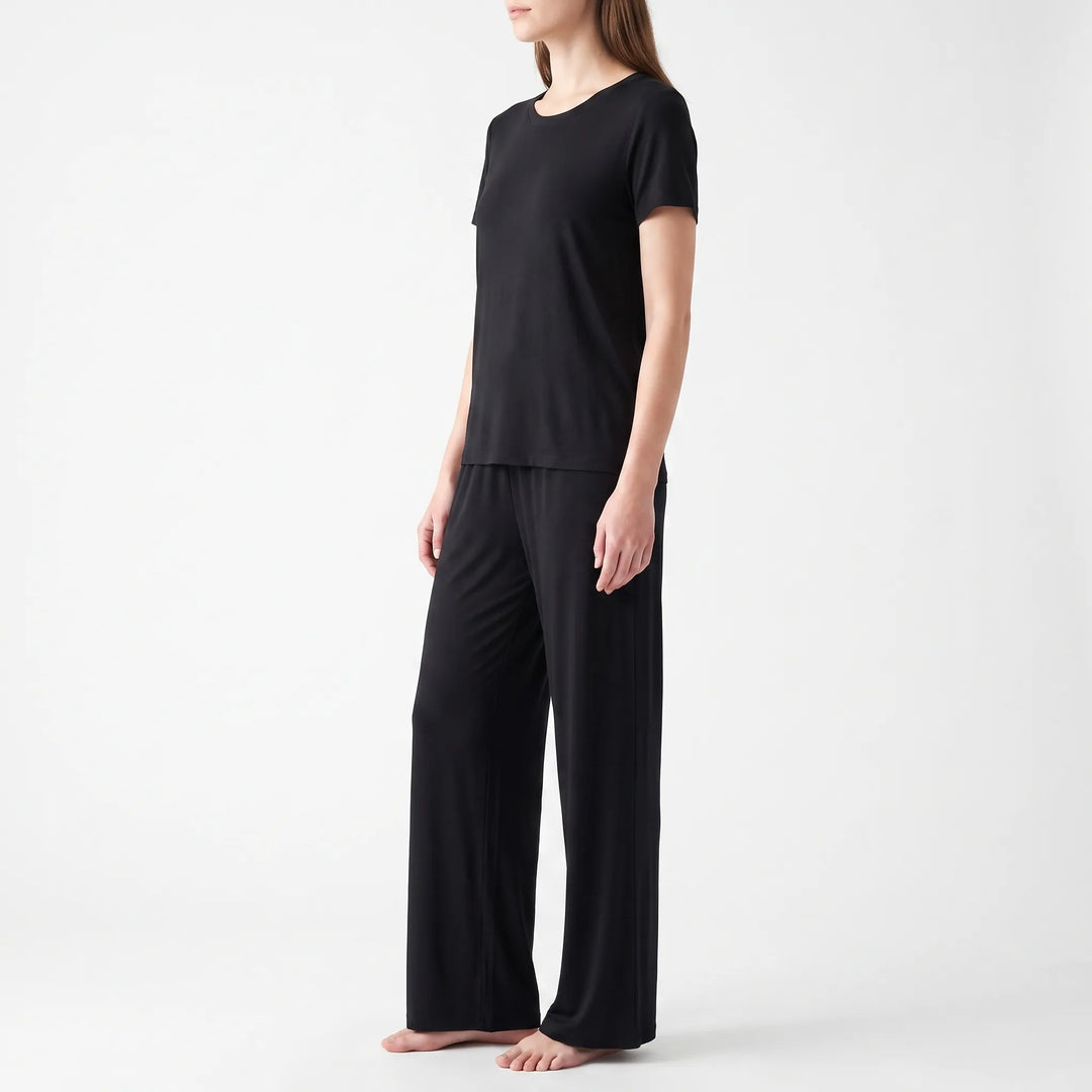 Side view of a model standing barefoot in the black short-sleeved top and wide-leg pants against a white background. 4