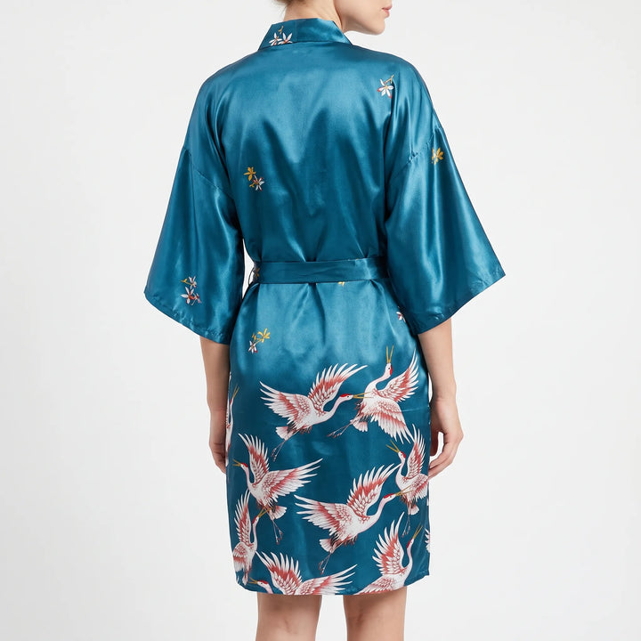Back view of the teal satin robe on a model, with crane print across the lower back and flowers on the collar. 3