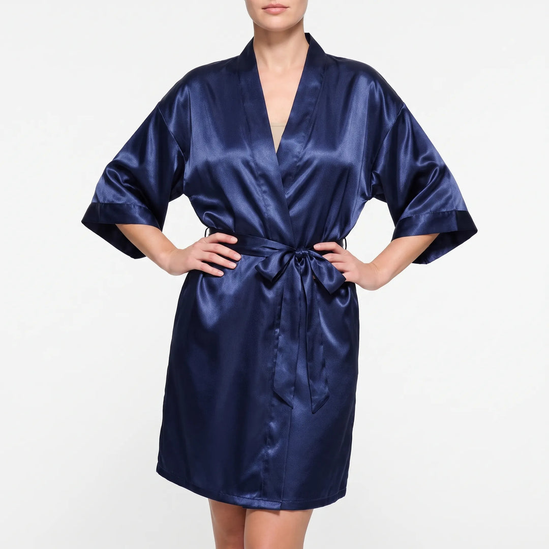 Front view of a model in a navy satin wrap robe with elbow-length sleeves, hands on hips and the belt tied in a bow. 2