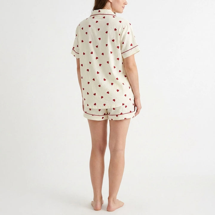 Back view of a model wearing the cream heart-print pajama shirt and shorts, showing the scattered red hearts and piped sleeve cuffs. 3