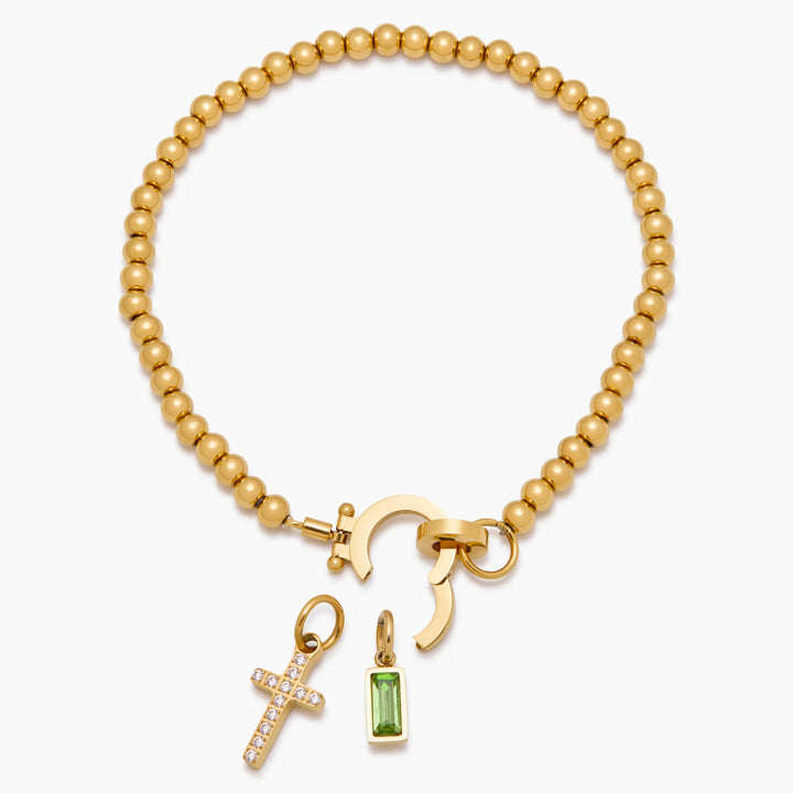 Gold-tone bead bracelet detail with the round clasp opened and the cross charm and green stone charm detached below it.