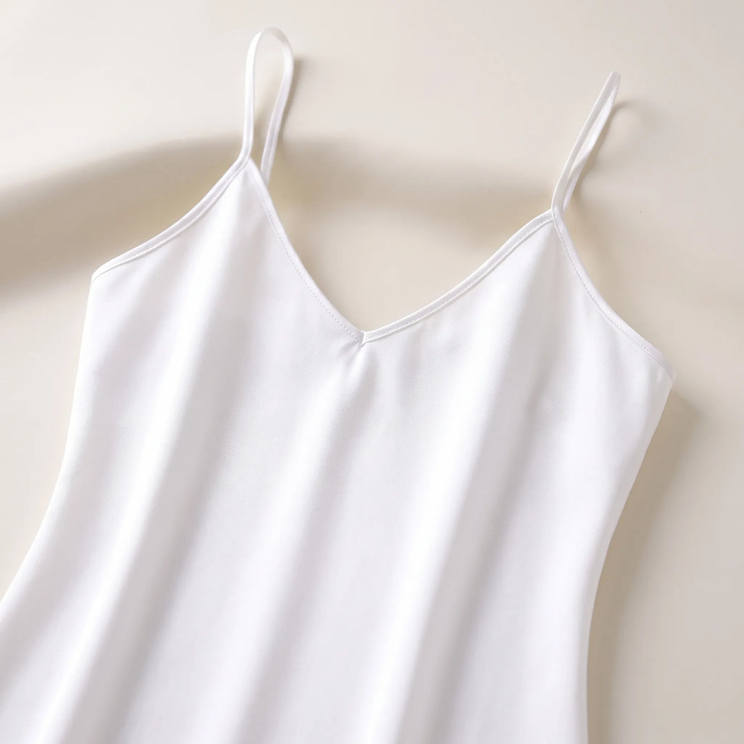 Close-up flat lay of the white slip's V-neckline, thin straps and stitched edging on a cream surface. 5