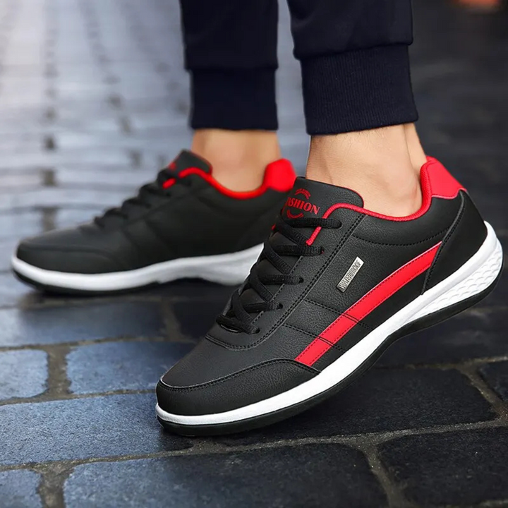 Black leather sneakers with red side stripes worn with dark joggers.
