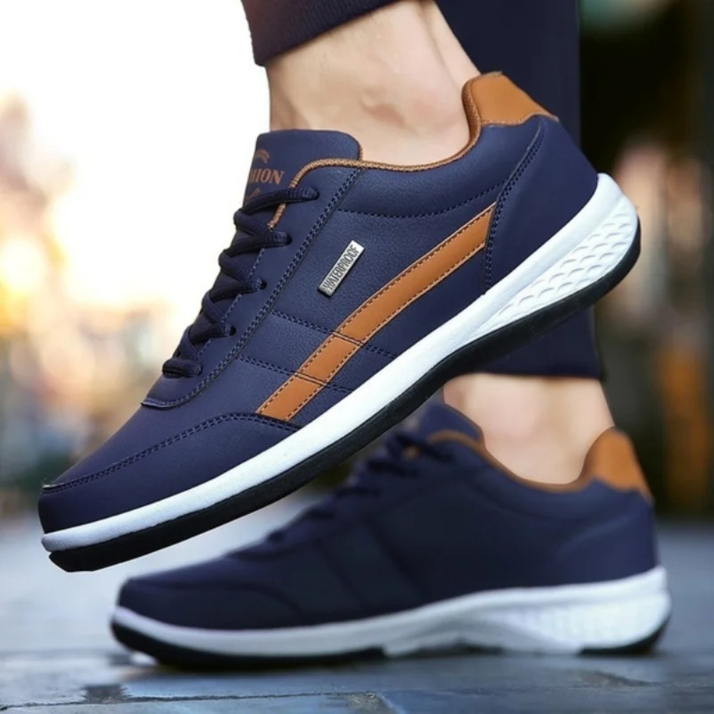 Navy leather sneakers with tan side stripes and white soles worn by a model.