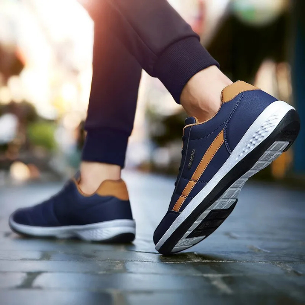 Rear three-quarter view of navy leather sneakers with tan heel tabs and patterned outsole tread.