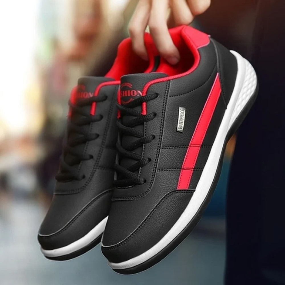 Black leather sneakers with a red side stripe and red collar held by hand.