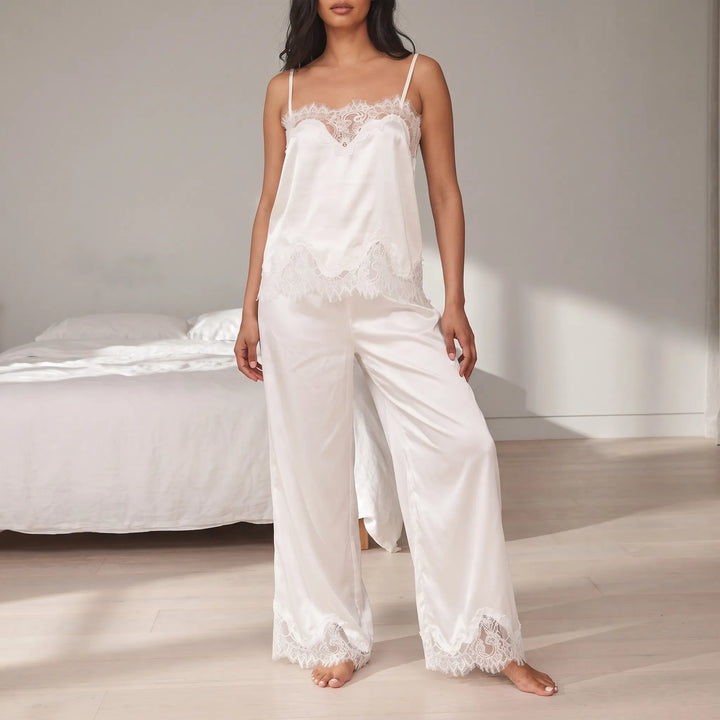 Model in a white satin cami and wide-leg pants with lace trim, standing barefoot in a bright bedroom. 1