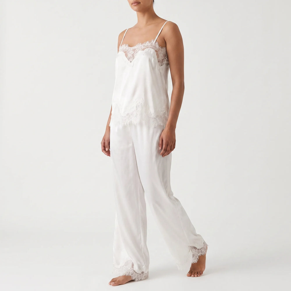 Studio shot of a model walking in the white satin cami and wide-leg pants, shown from a three-quarter front angle. 2