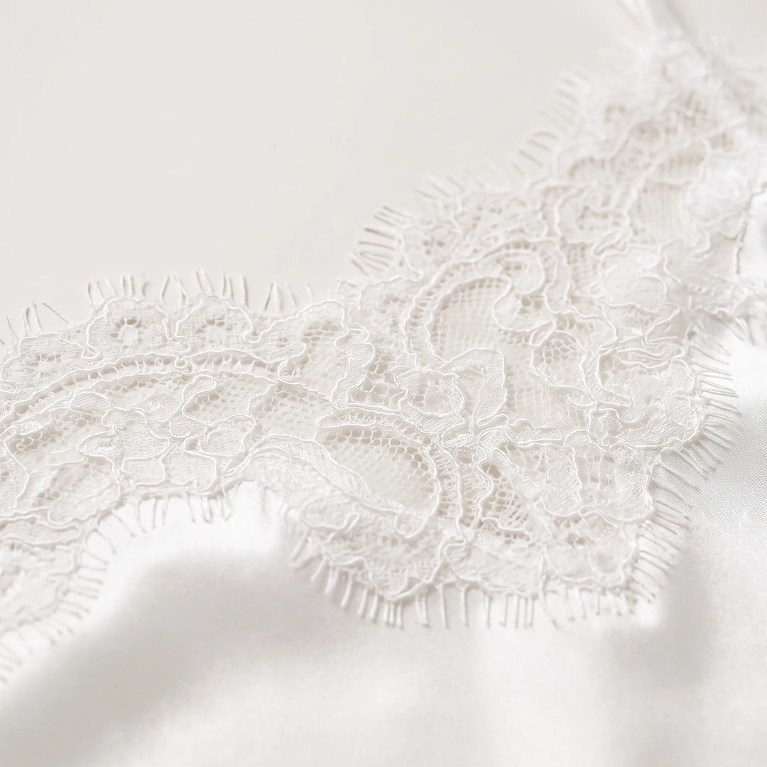 Close-up detail of the delicate white eyelash lace trim resting against smooth, glossy white satin fabric. 5