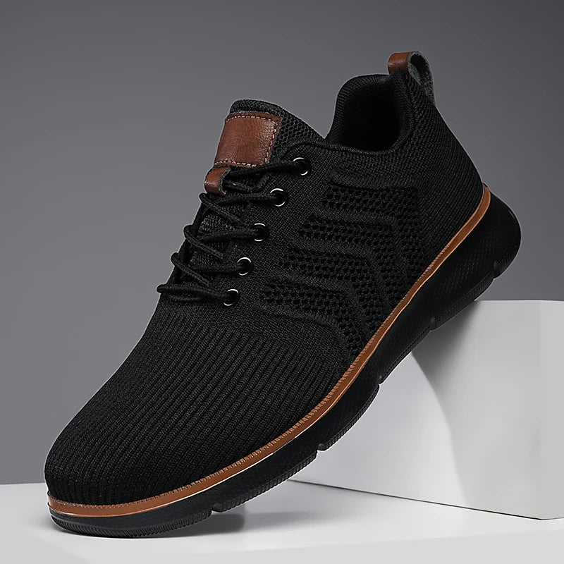 Close-up side view of a black sneaker with a black sole and tan leather tongue patch.