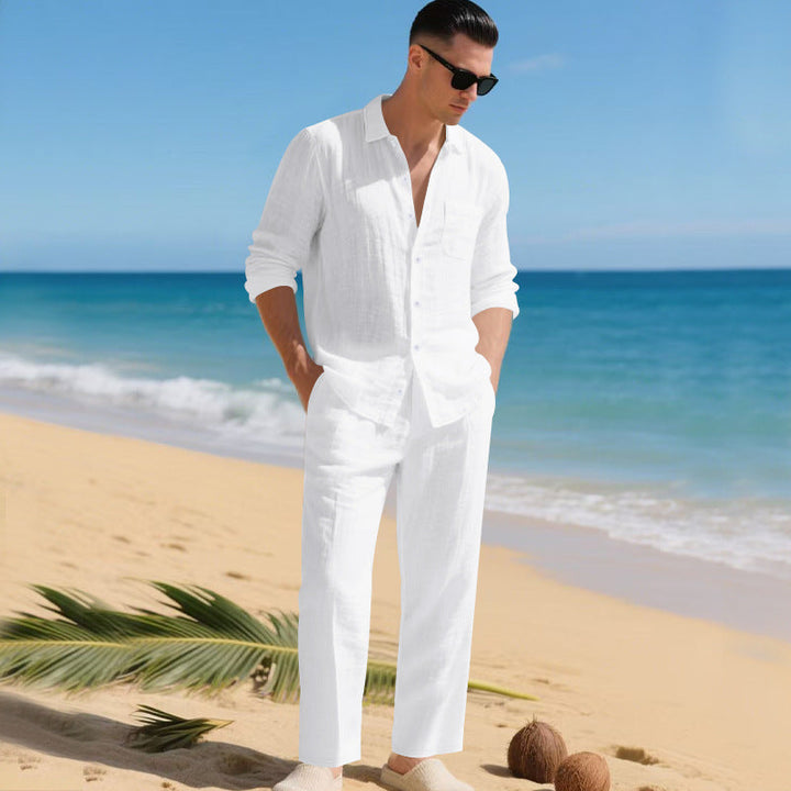 Men's linen shirt and pants set in all-white on a model at the beach, another view.