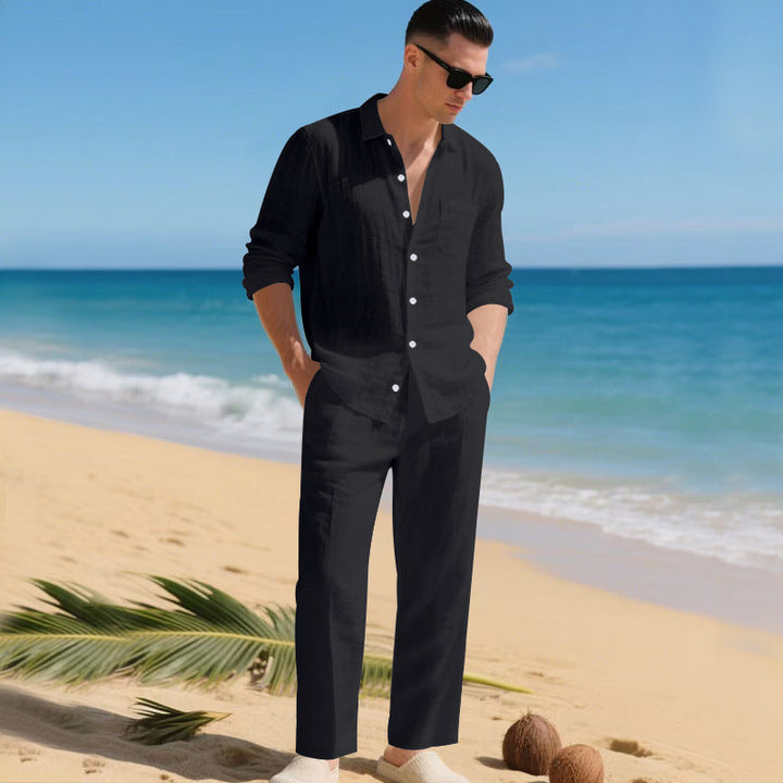 Men's linen shirt and pants set in black on a man on a sandy beach, front view.