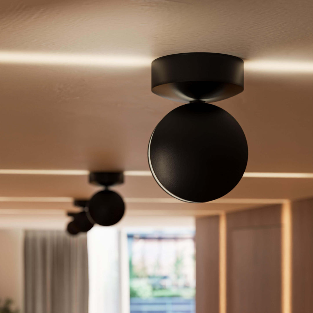 Black LED wall sconce detail showing a round-headed spotlight with thin beams on the ceiling.