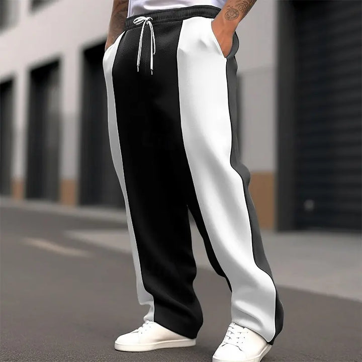 Model outdoors wearing black and white color-block sweatpants with a white drawstring, hand in pocket, white sneakers 2