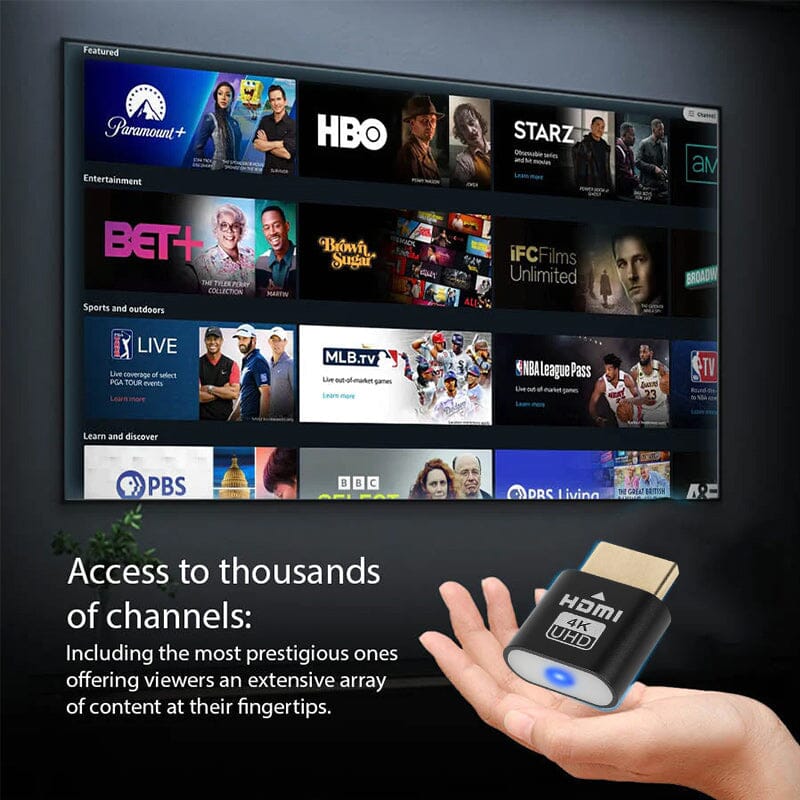 Black dongle held in front of a wall-mounted TV showing a menu of streaming channel tiles