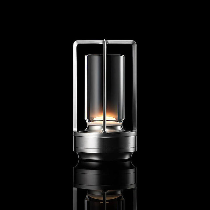 Silver-finish lamp with open frame and clear glass cylinder, softly lit against a black background with reflection.