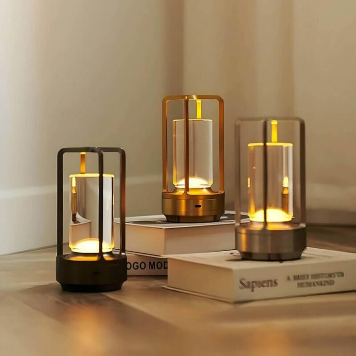 Three lamps in black, gold and silver finishes glowing warmly on stacked books and a wood floor in a room corner.