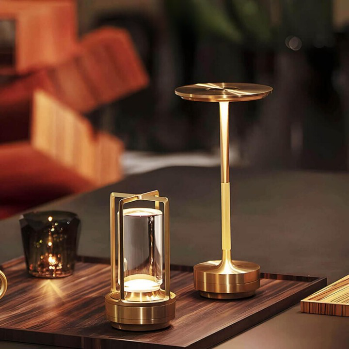 Gold cylinder lamp on a wooden tray beside a taller gold mushroom-style table lamp, in a cozy lounge.