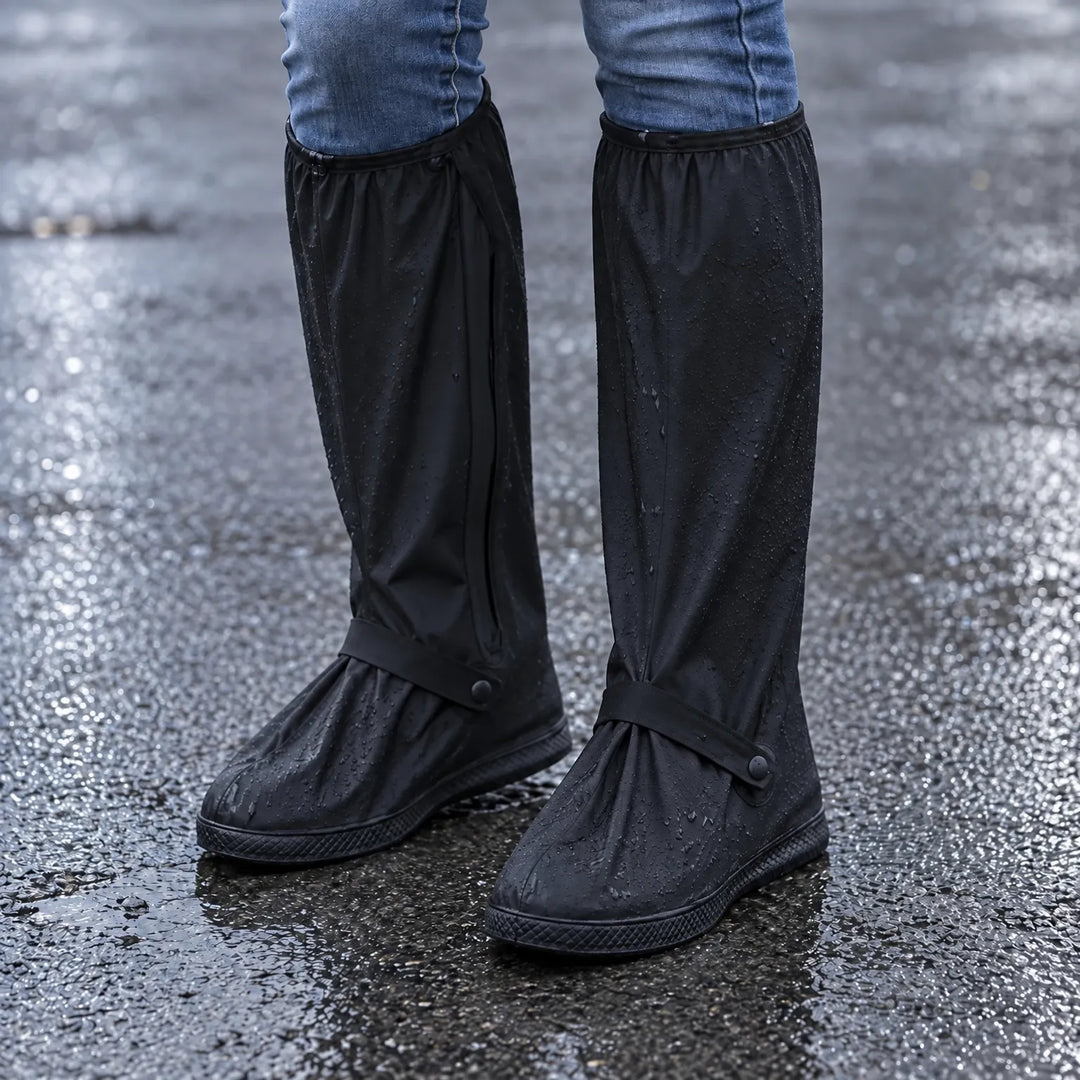 Black knee-high rain shoe covers with ankle straps worn with jeans on wet asphalt, water droplets beading on the fabric. 1