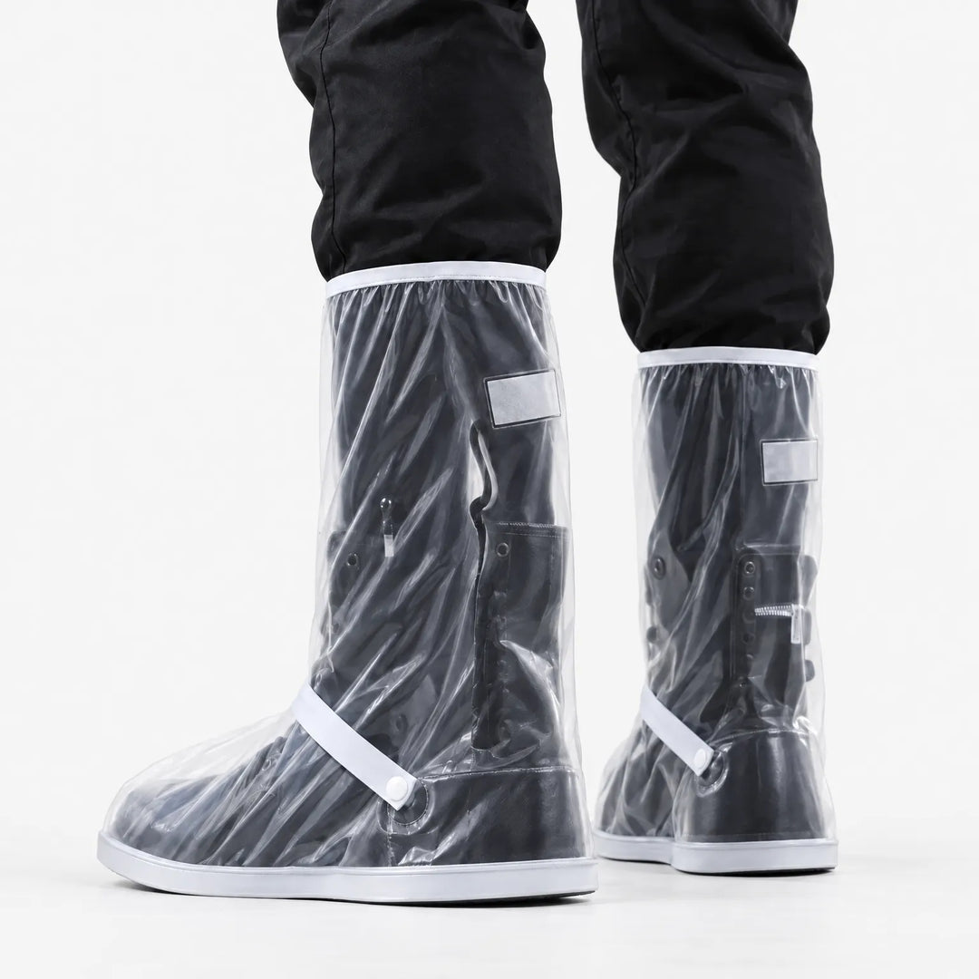 Rear three-quarter view of clear tall shoe covers worn over black boots, showing the reflective patch, ankle strap and snap button. 4