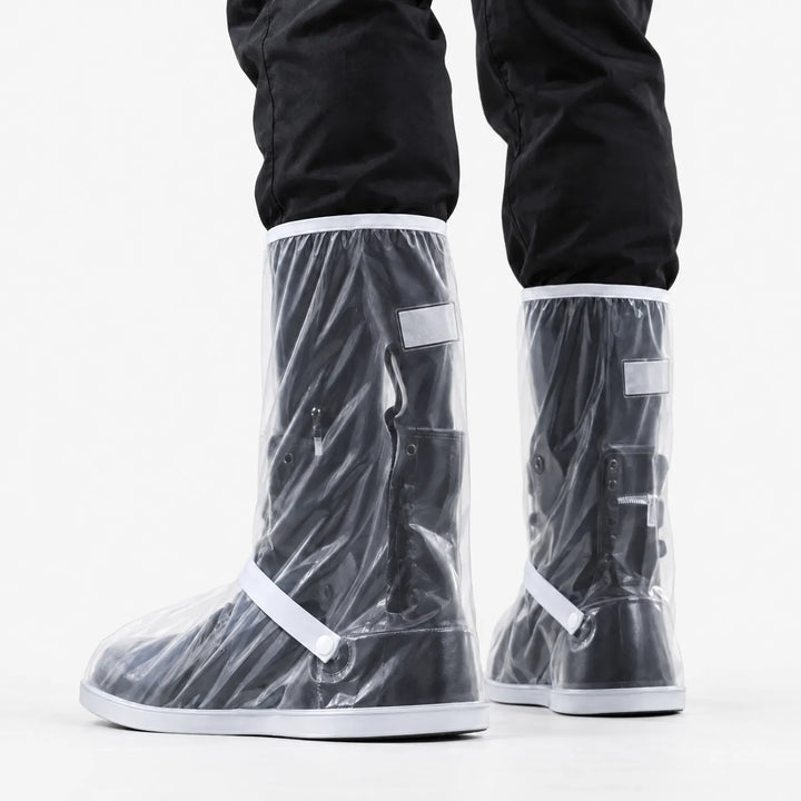 Rear three-quarter view of clear tall shoe covers worn over black boots, showing the reflective patch, ankle strap and snap button. 4
