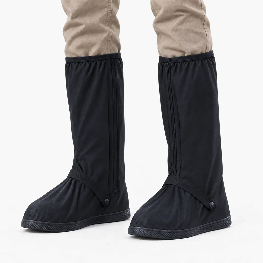 Front view of black tall shoe covers with side zippers and ankle straps, worn with khaki pants against a white background. 7