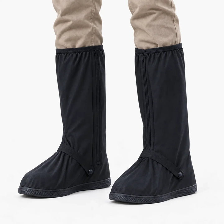 Front view of black tall shoe covers with side zippers and ankle straps, worn with khaki pants against a white background. 7