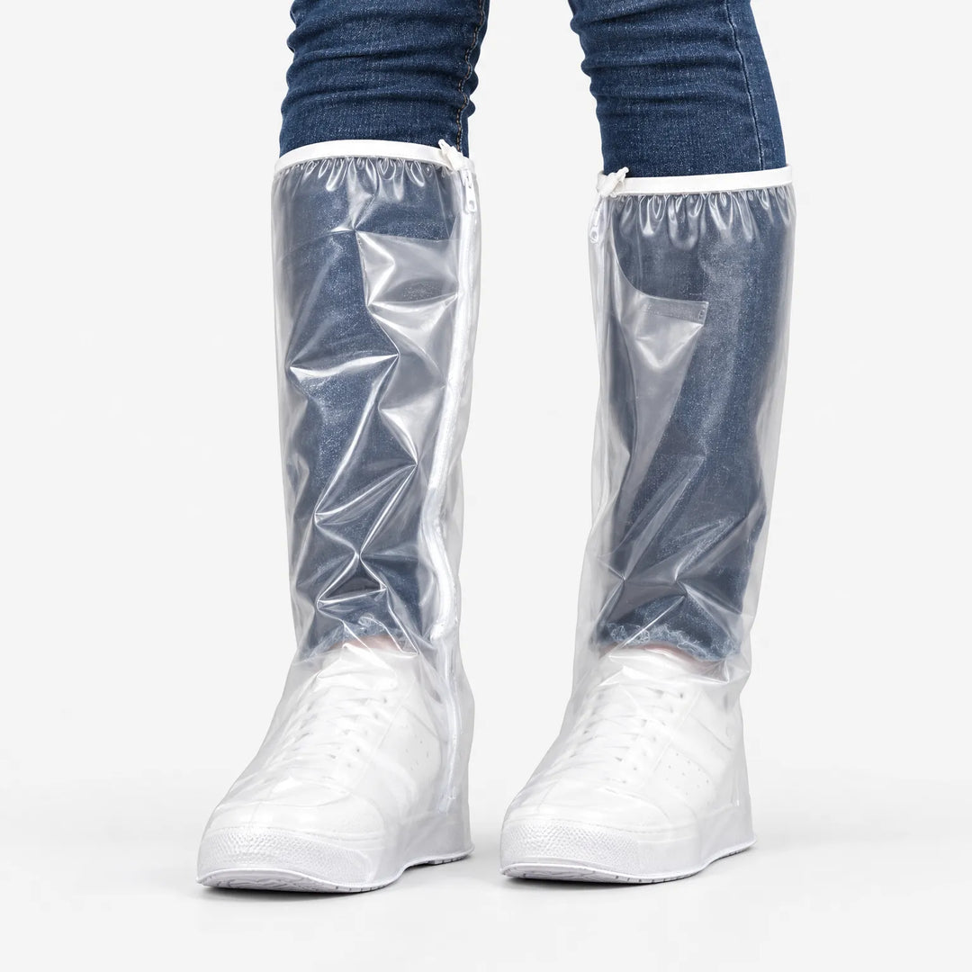 Front view of clear tall overshoes with a side zipper and white trim, worn over white sneakers and jeans against a plain background. 2