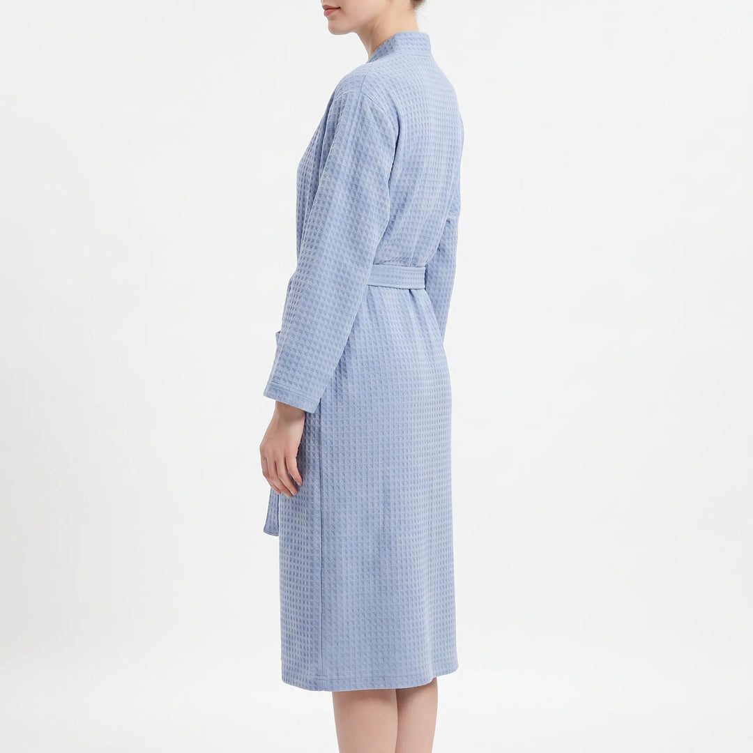 Side profile of a model wearing the light blue waffle-weave robe, showing the long sleeve, belt and knee-length hem. 4