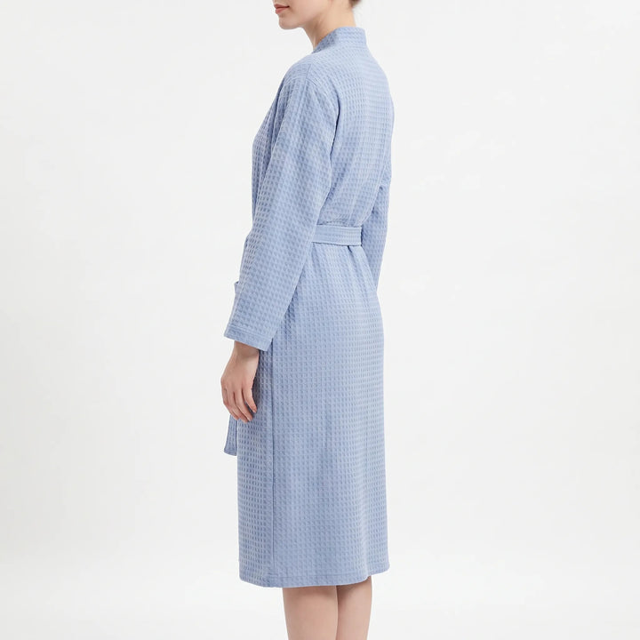 Side profile of a model wearing the light blue waffle-weave robe, showing the long sleeve, belt and knee-length hem. 4