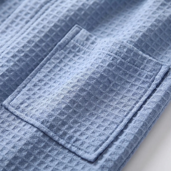 Close-up of a stitched patch pocket on blue waffle-weave fabric, showing the raised grid texture of the weave. 5
